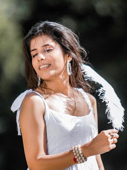 A lovely solo portrait of the bride in a sun-dappled forest. She holds a white feather, adding a touch of delicate, whimsical detail to this natural and serene photograph.