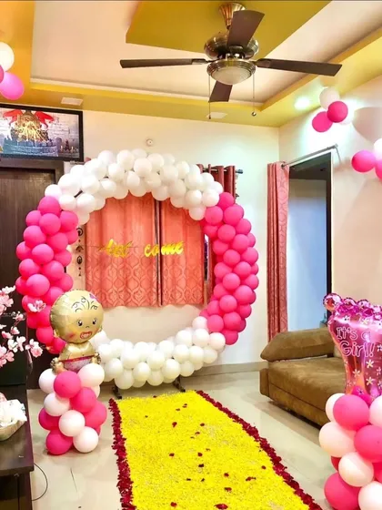 A beautiful welcome home decoration featuring a large ring of pink and white balloons and a flower petal carpet. This setup is perfect for creating a stunning photo opportunity as you bring your baby girl home.