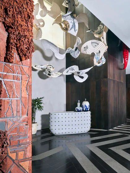 Our curation extends to every part of a home, including this distinctive bar area. Here, a contemporary bar from Scarlet Splendour is juxtaposed with a raw, textural terracotta wall map by Pravat M and a floating paper installation, demonstrating our eclectic approach to material and form.