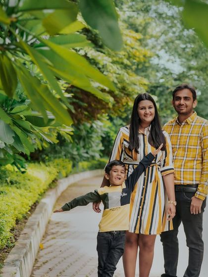 A playful family portrait in the park. The son's fun pose adds a touch of personality and energy to this happy family photo.