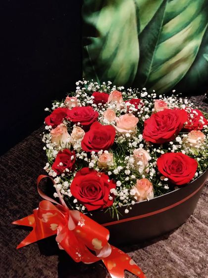 A classic expression of love. This heart-shaped box is filled with romantic red and pink roses and a cloud of baby's breath, tied with a festive red ribbon.