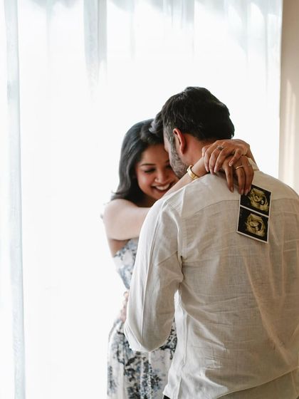 A happy, candid moment between a couple in a simple, patterned dress and shirt, using the sonogram for a sweet reveal.