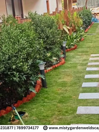 The finished backyard in Bommenahalli, featuring a healthy natural lawn bordered by layered ornamental plants. The stone pathway provides a clean and practical walkway through the garden.