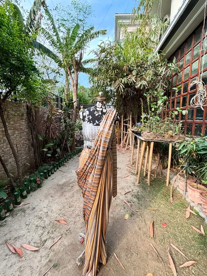 A wide shot of our striped saree in a beautiful garden setting. The natural fabric and colors blend perfectly with the surroundings.