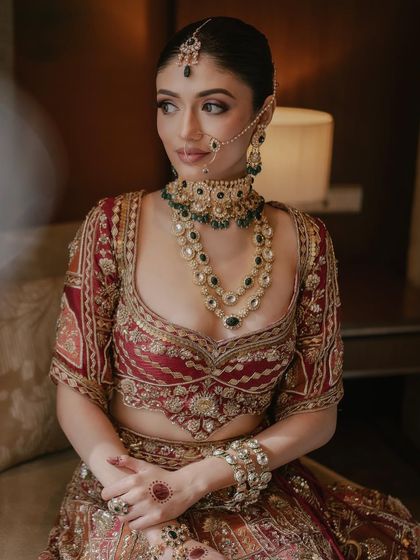 A traditional bridal look with a modern touch. The deep red lehenga and layered jewelry are paired with a clean, defined makeup look that feels both classic and current.