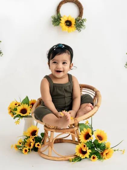 A sunny sunflower-themed first birthday! This happy baby is surrounded by bright yellow flowers, sitting in a cute rattan chair for her milestone portrait.