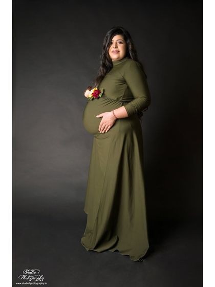 A full-length studio portrait in a simple olive green dress. The small floral detail on the bump adds a beautiful, organic touch to the classic pose.