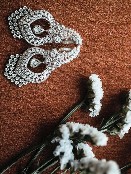 An artistic close-up of a pair of diamond earrings resting on a textured surface with delicate white flowers.