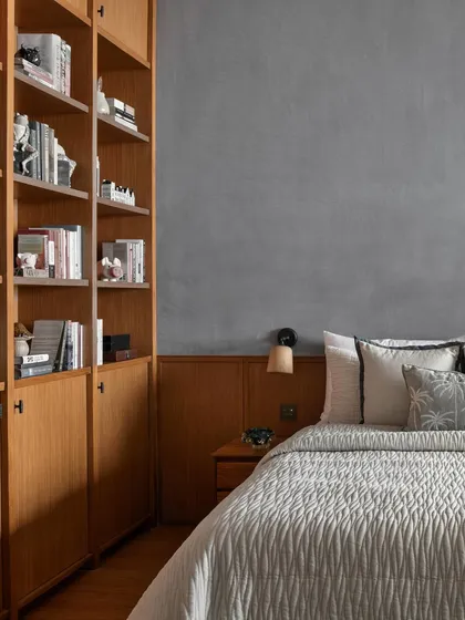Designed as a personal retreat for a resident who loves reading, this bedroom features a wall of custom bookshelves. The muted blue-grey stucco wall provides a calming backdrop to the warmth of the wooden paneling and book collection.