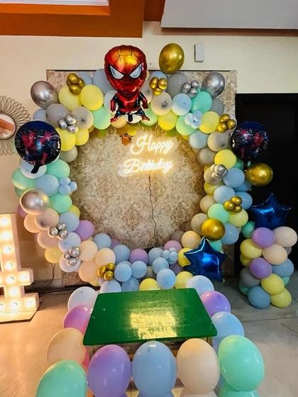 A fun Spiderman theme for a 4th birthday. This setup features a circular balloon arch in pastel colors, Spiderman foil balloons, a neon sign, and a light-up number '4'.
