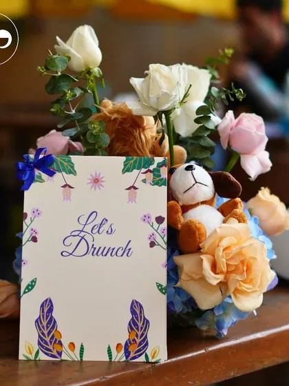 A 'Let's Drunch' menu card sits amongst a beautiful floral arrangement with soft-hued roses and hydrangeas.