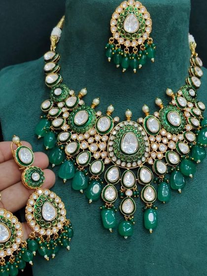 A beautiful green beaded Kundan necklace set held in hand to show the details. This rental set includes a maang tikka and earrings.