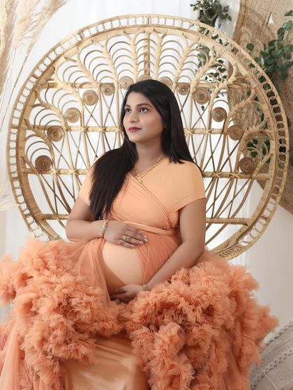The feeling is divine. This mom-to-be looks thoughtful and serene, seated on a peacock throne in a beautiful peach ruffled gown.
