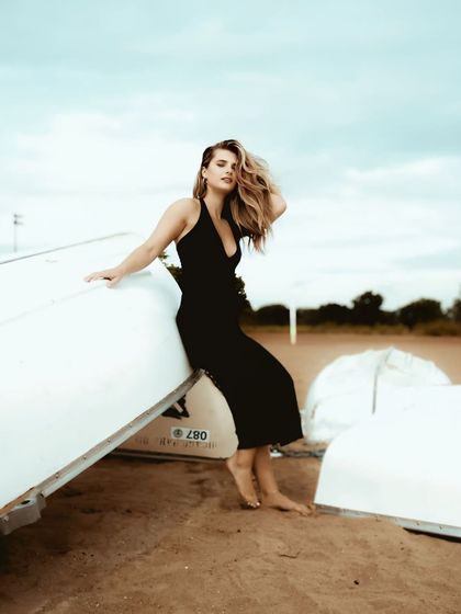 A stylish portrait on the sands of Goa, with the model leaning against overturned white boats, creating a clean and minimalist beach aesthetic.