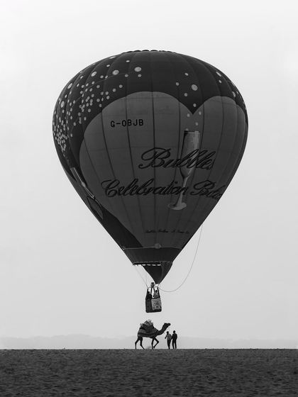 A hot air balloon appears to be tethered to a camel in this cleverly composed black and white shot from the Varanasi balloon festival, playing with scale and perspective.