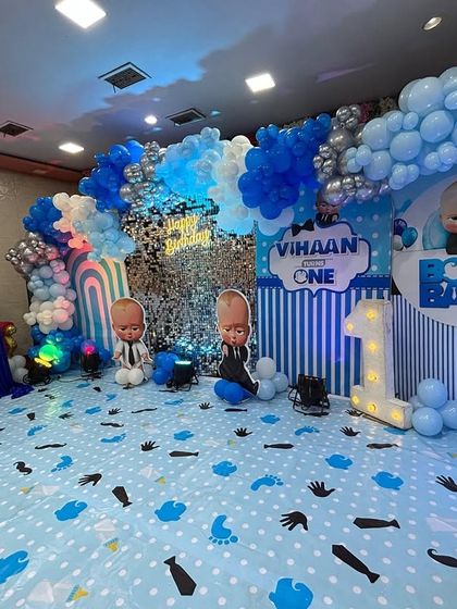A fun Boss Baby theme for Vihaan's first birthday. The setup includes a custom printed floor mat, multiple character cutouts, and a blue, silver, and white balloon arch.
