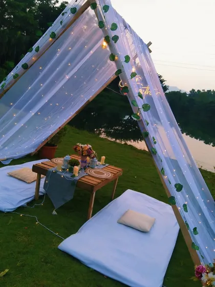 The simple elegance of the picnic setup, with sheer white drapes and delicate leaf garlands, creates a dreamy and peaceful setting for an anniversary celebration.