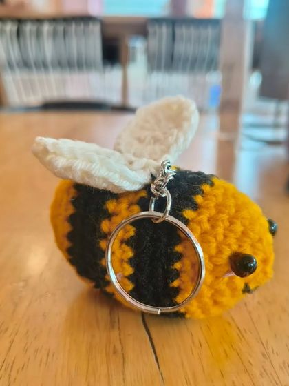 A simple, sweet shot of a single crochet bee keychain resting on a wooden table. You can really see the quality of the stitches here.