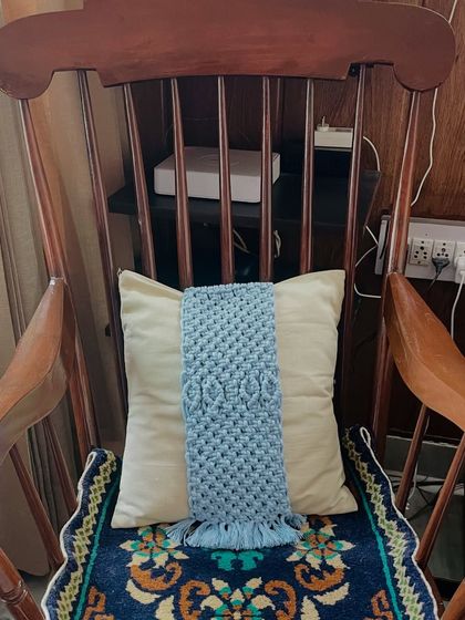 Here is the same blue tie-back shown on a cushion placed in a classic wooden rocking chair. It demonstrates how these accessories can add a touch of personalized, cozy charm to any seating area in your home.