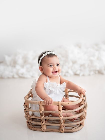 A smiling baby girl in a basket, a classic and adorable pose for a sitter session.
