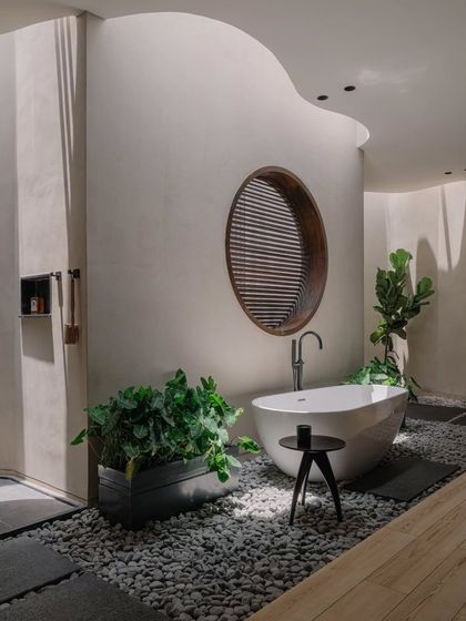 This master bathroom breaks from the home's linear geometry with its curved walls and organic layout. A freestanding tub sits on a bed of pebbles, creating a spa-like, earthy atmosphere.