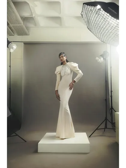 A sleek, white long-sleeved gown by Rudraksh Dwivedi. The styling is clean and powerful, with puff sleeves and embellished details adding a touch of regality.