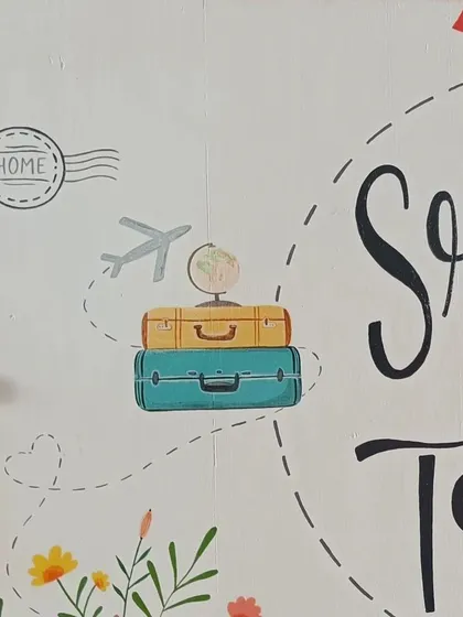 A duplicate of 70, detail shot of the travel-themed name board, showing the hand-painted suitcases, globe, and airplane, capturing the couple's wanderlust spirit.