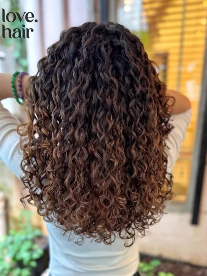Adding dimension with a brunette balayage. These lighter pieces are strategically placed to catch the light and make the curls pop without a full head of colour.