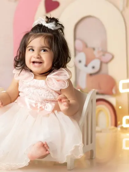 A princess in her throne. This little one is all smiles in her beautiful pink dress, celebrating her first birthday.