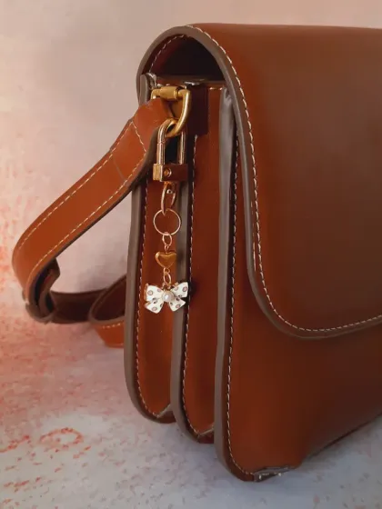 A side view of the white enamel bow and heart bag charm, demonstrating its delicate size and how it hangs elegantly from a bag.