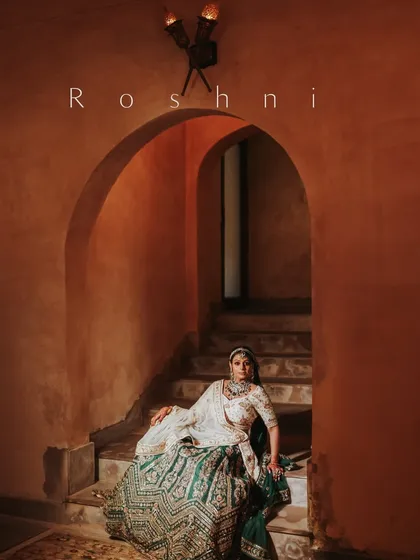 A royal bridal portrait. The bride is seated on a staircase in a palace, her intricate lehenga and regal pose creating an image of timeless elegance.