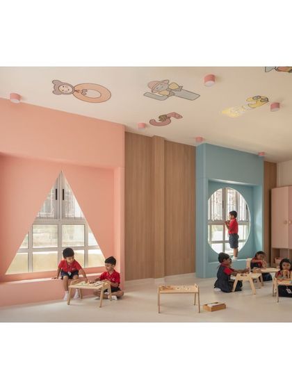 This classroom features unique architectural details like large, shaped window nooks that double as cozy reading spots. The mix of pink and blue tones creates a soft, playful environment for young learners.