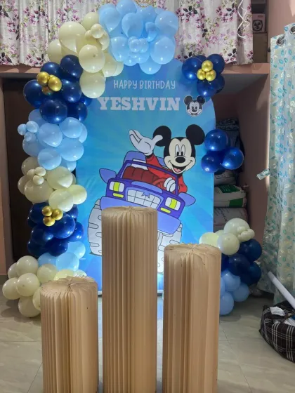 A Mickey Mouse-themed birthday for Yeshvin. The setup includes a custom arched backdrop with Mickey in a monster truck, framed by a blue and gold balloon garland.