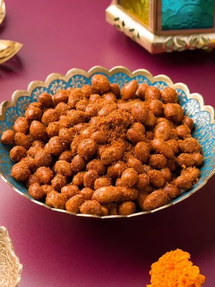 Spiced peanuts in a colorful bowl, surrounded by marigold flowers and diyas. The composition is rich with festive details.