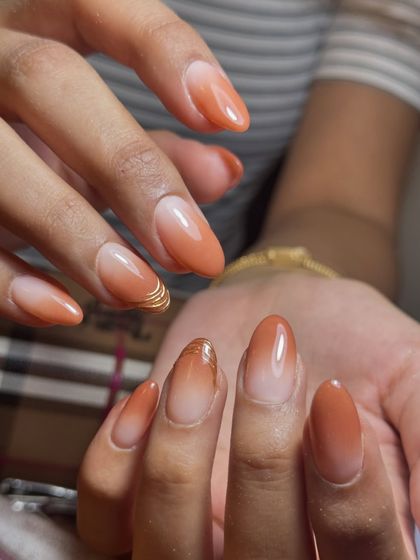 A full view of the warm, peachy ombré nails with a delicate gold accent.
