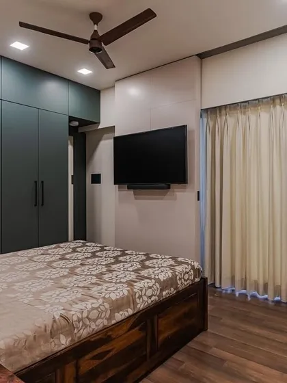 This bedroom demonstrates several integrated features. The wardrobe in rich highland green includes an open shelving unit, and next to it, a sliding TV unit conceals a full-size mirror, showcasing our holistic design approach.