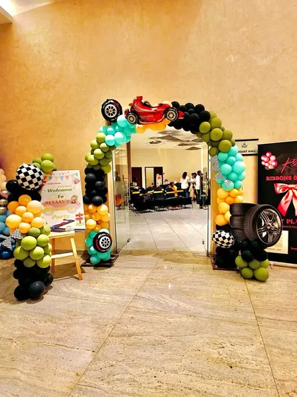 The entrance to Avyaan's car-themed party, with a vibrant balloon arch, tire props, and a welcome sign to greet the guests.
