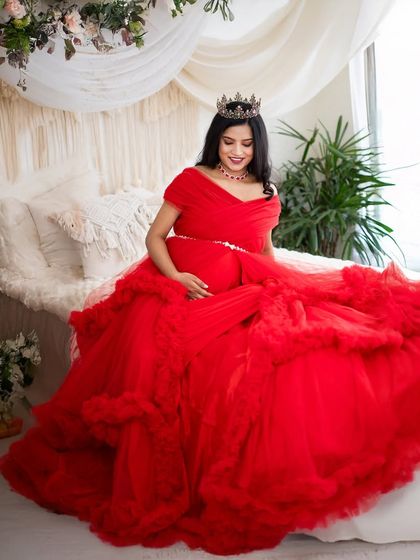 A moment of quiet reflection on our studio bed. The mom-to-be, dressed in a stunning red gown and crown, creates a peaceful and beautiful image.