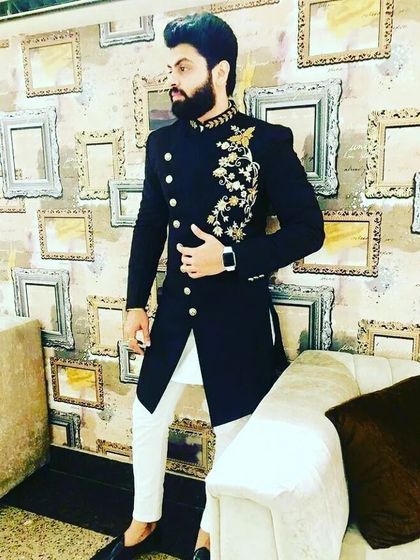 A sharp black Indo-western sherwani with asymmetrical buttons and gold embroidery on the shoulder. Paired with white trousers, this outfit is perfect for a cocktail party or reception.
