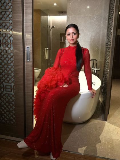 The full look is pure glamour. The dramatic red dress with ruffled sleeves is perfectly balanced by the sleek hair and bold makeup.