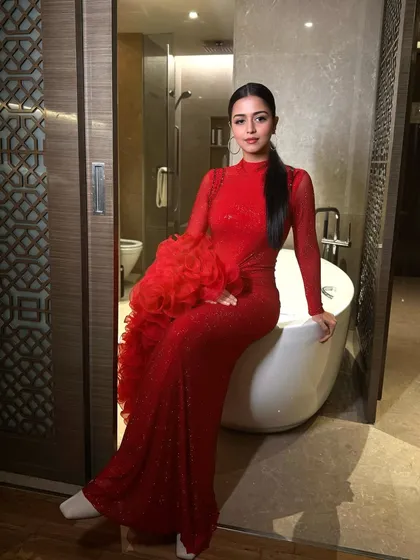 The full look is pure glamour. The dramatic red dress with ruffled sleeves is perfectly balanced by the sleek hair and bold makeup.