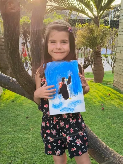 A happy artist with her finished penguin painting, featuring a lovely blue background.
