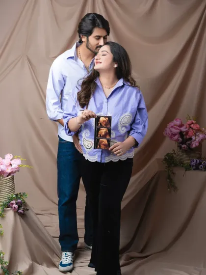Sharing a special secret. The couple holds their ultrasound photo, their expressions full of love and happiness in this casual and sweet portrait.