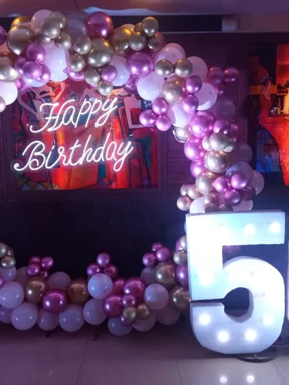 Celebrating a 50th birthday with flair, this full balloon ring is packed with metallic pink, gold, and white balloons. Paired with large light-up marquee numbers, this setup creates a bright and celebratory focal point, especially for evening events.