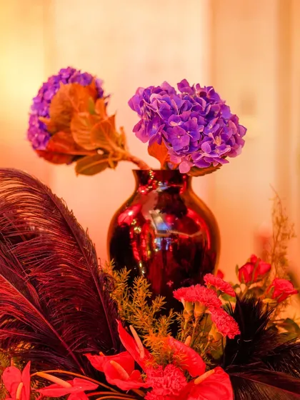 A small but striking detail of a purple hydrangea in a dark red vase, placed next to black feathers. This shows the eclectic mix of colors and textures used in the theme.