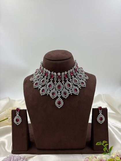 A heavy, silver-plated AD necklace set with a peacock-inspired feather design. This statement piece is available in blue, green, pink, and all-white.