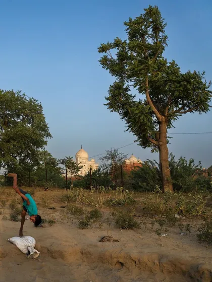 A young boy does a handstand in the fields near the Taj Mahal, a moment of playful acrobatics against a world-famous backdrop.