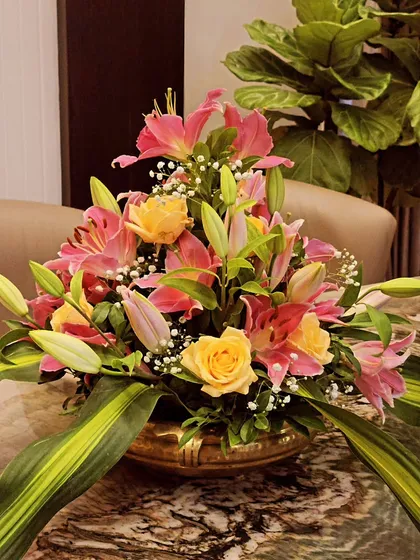 A beautiful flower arrangement in a brass urli, with pink lilies and yellow roses. This is perfect as a centerpiece for any event.