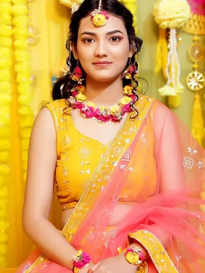 A beautiful portrait of the bride during her Haldi ceremony, radiant in her yellow and pink outfit against a vibrant floral backdrop.