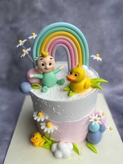 A whimsical Cocomelon cake featuring JJ and his ducky friend under a pastel rainbow. The hand-painted daisies and fluffy fondant clouds add a touch of sweetness to this adorable design.